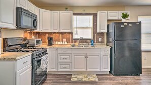 A kitchen with white cabinets, a black refrigerator, a stove, a microwave, and a sink.
