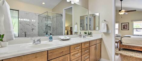 A modern bathroom with a large mirror, dual sinks, wooden cabinets, and a ceiling fan.