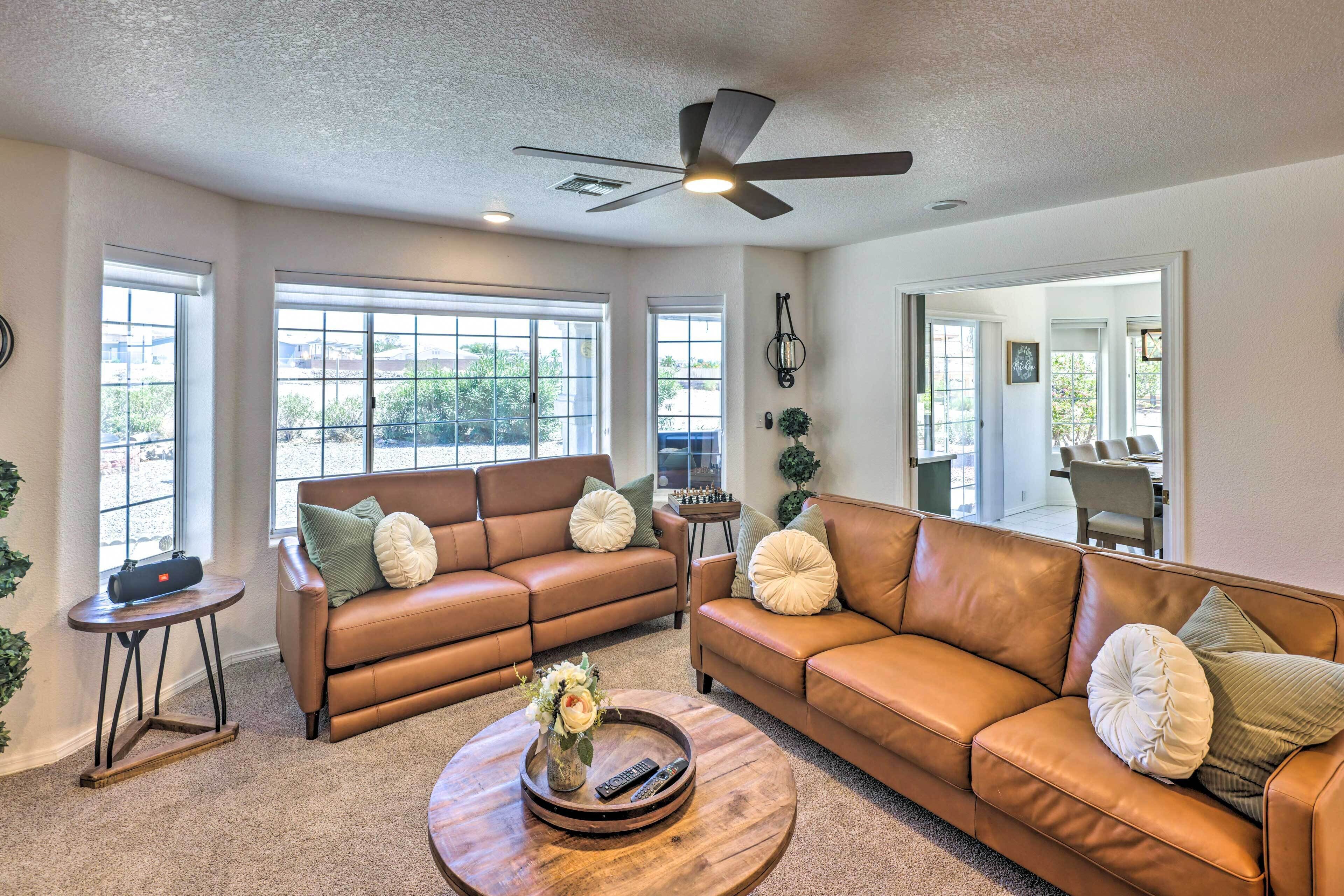 A spacious living room with leather sofas, a coffee table, and large windows.