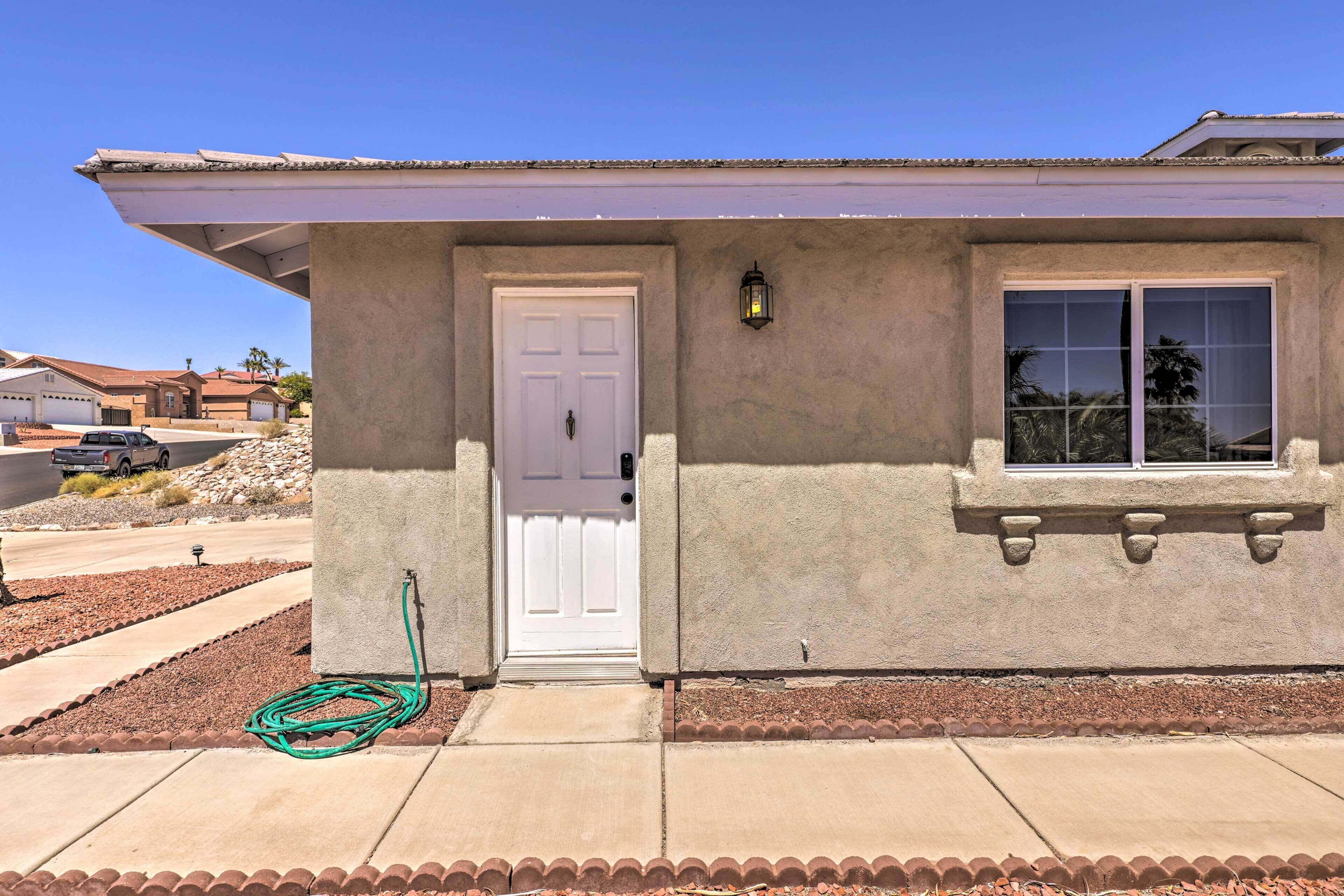 A single-story house with a white door, a window with a stone frame, and a green hose on the ground.