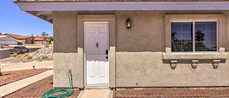A single-story house with a white door, a window with a stone frame, and a green hose on the ground.