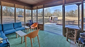 Een overdekt terras met een blauwe bank, oranje stoelen en een houten tafel.