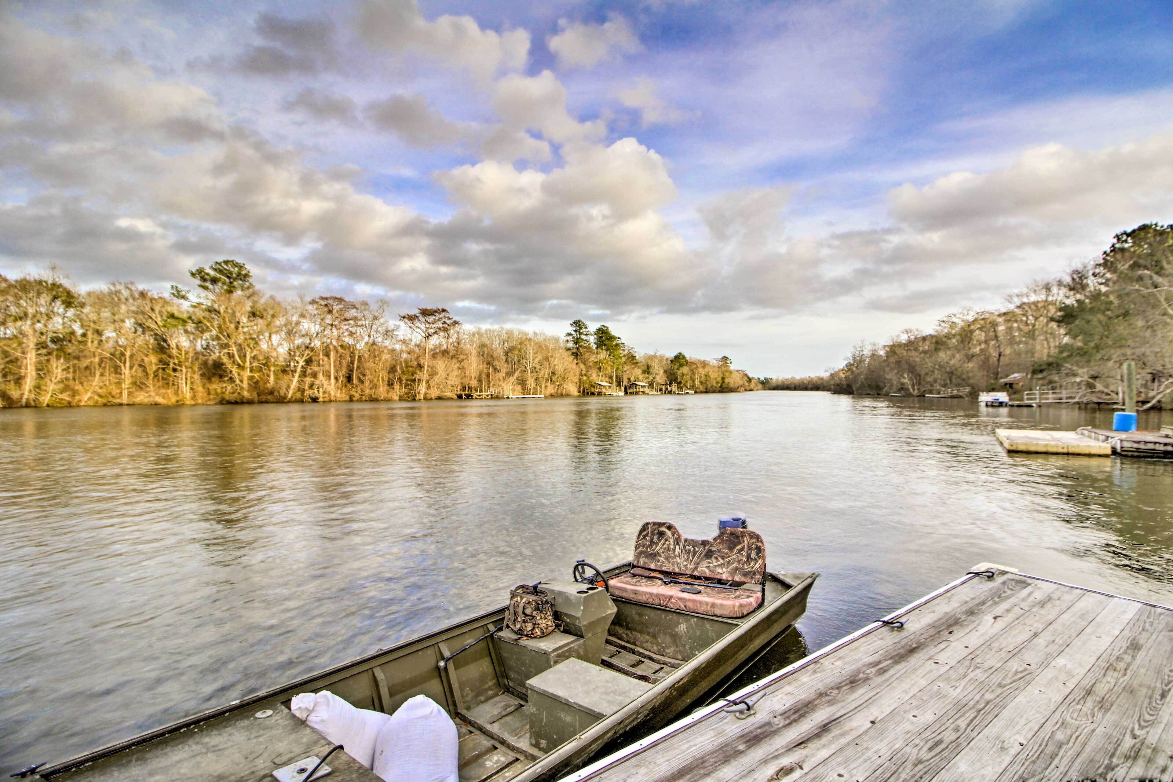 A wooden dock extending into a calm river with a boat moored at the end.