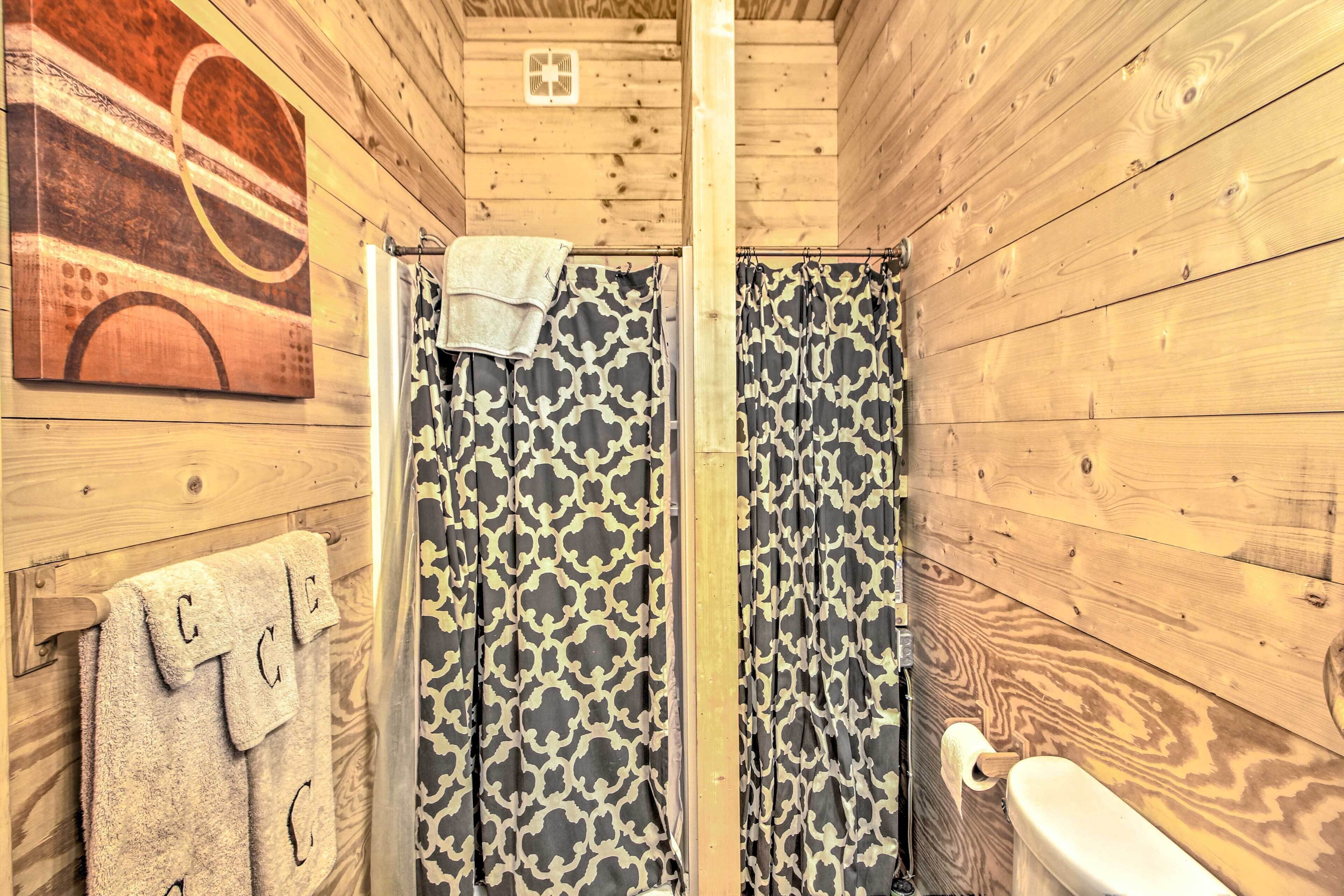 Une salle de bain rustique, aménagée dans une cabane en bois, avec un rideau de douche, des toilettes et une serviette accrochée au mur.