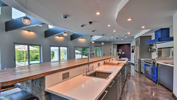 A modern kitchen with a long island, stainless steel appliances, and a view of the outdoors. - Southern Shores Retreat w/ Expansive Outdoor Space (Kitty Hawk)