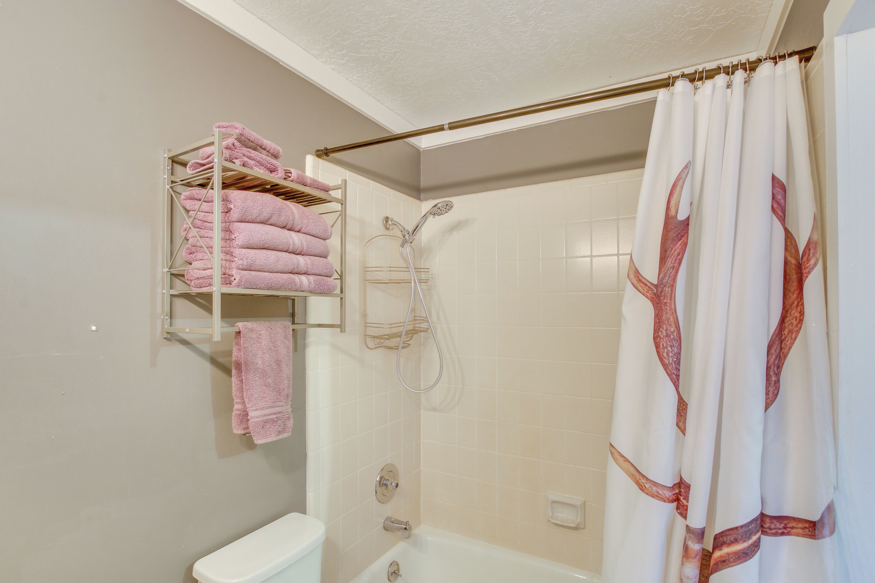 Een badkamer met een douche, toilet en een handdoekrek met roze handdoeken.