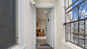 Un couloir étroit, avec une porte sur la gauche et une rambarde métallique sur la droite.