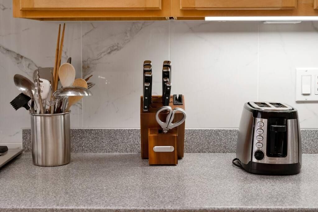 A kitchen counter with a stainless steel utensil holder, a wooden knife block, and a toaster.