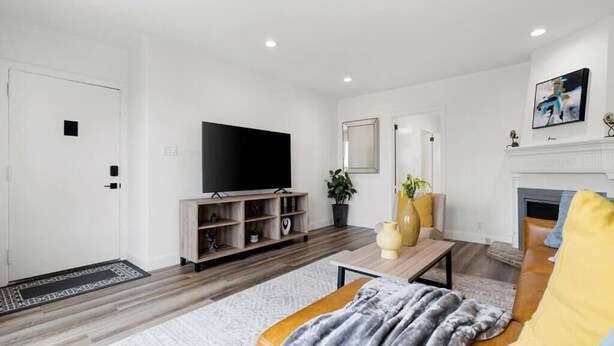 Un salon moderne doté d’un téléviseur à écran plat, d’un plancher en bois, d’un canapé, d’une table basse et d’une cheminée.