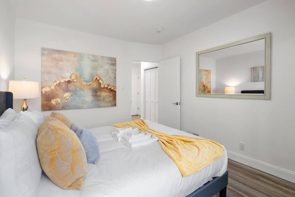 Un cuarto de hotel con una cama, un cuadro abstracto grande, un espejo y una lámpara.