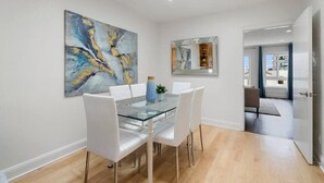 Un espace repas avec une table en verre, des chaises blanches et un grand tableau abstrait.