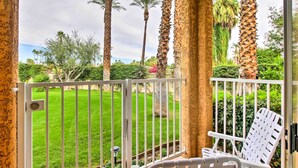 A balcony with a white chair, a view of a well-maintained lawn, and tall palm trees. - Pool & Hot Tub Access: Modern Palm Springs Condo (Palm Springs)