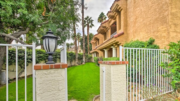 A gated entrance with a well-maintained lawn, a lamp post, and a building with a stucco exterior and balconies. - Pool & Hot Tub Access: Modern Palm Springs Condo (Palm Springs)