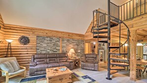 A log cabin interior with a spiral staircase, leather sofas, a wooden coffee table, and a patterned rug. - 2 Decks & Fire Pit: Scenic Beech Mountain Retreat! (Banner Elk)