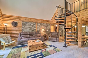 A log cabin interior with a spiral staircase, leather sofas, a wooden coffee table, and a patterned rug.
