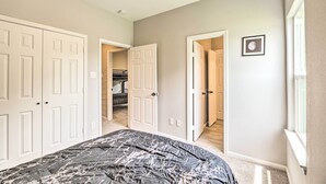 Une chambre avec un grand lit, deux portes blanches, un placard et un couloir menant à une autre pièce.
