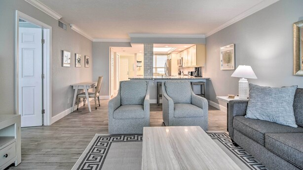 A living room with a sofa, two armchairs, a coffee table, and a rug. There is a door on the left and a kitchen in the background. - Remodeled Redington Shores Gem on the Beach! (Redington Shores)