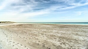 A wide sandy beach with visible footprints, a clear sky, and a distant shoreline. - Remodeled Redington Shores Gem on the Beach! (Redington Shores)