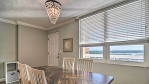 A dining room with a large wooden table, white chairs, a chandelier, and a window with blinds. - Remodeled Redington Shores Gem on the Beach! (Redington Shores)