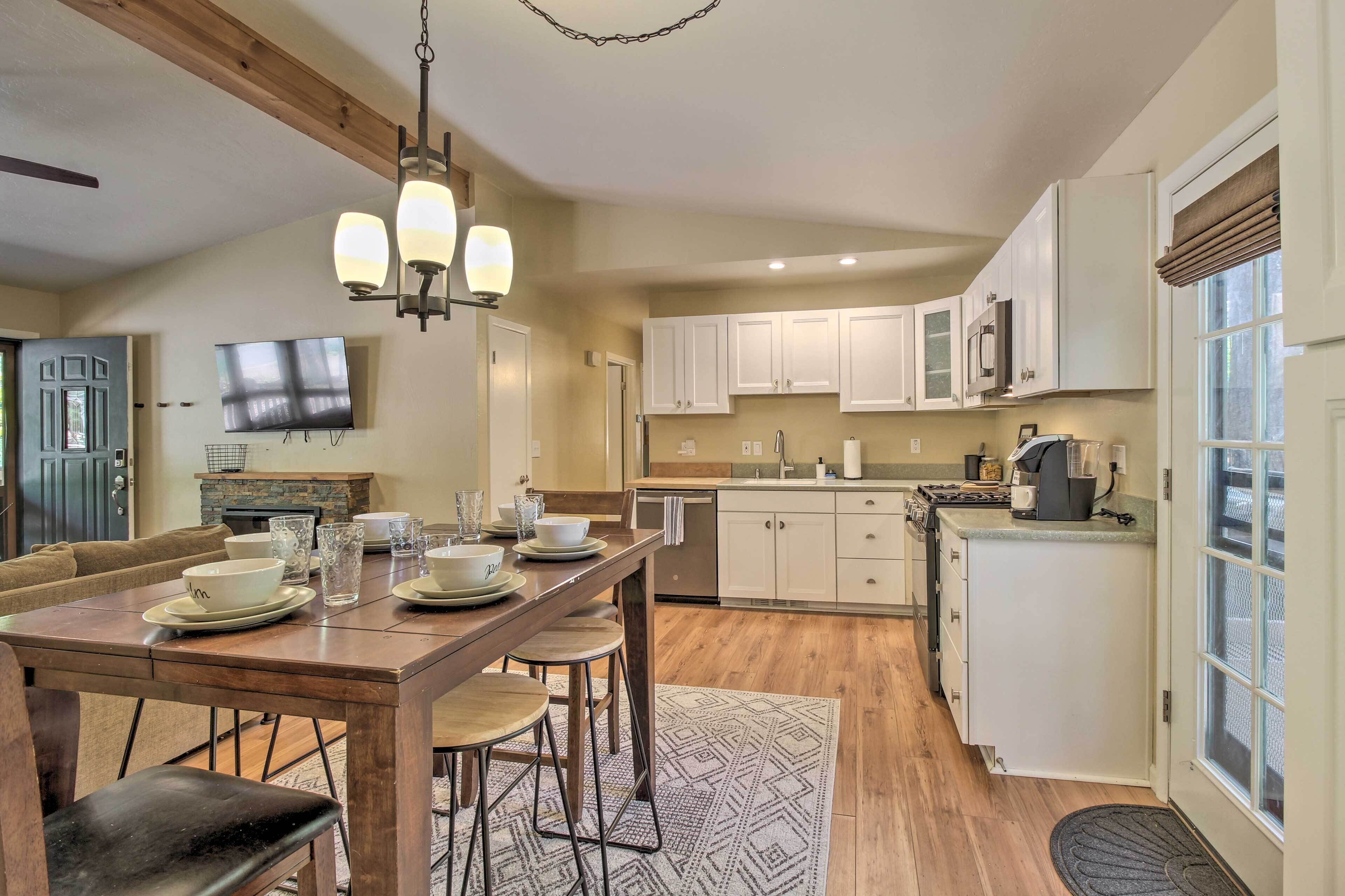 A modern kitchen with white cabinets, a wooden dining table, and a TV mounted on the wall.