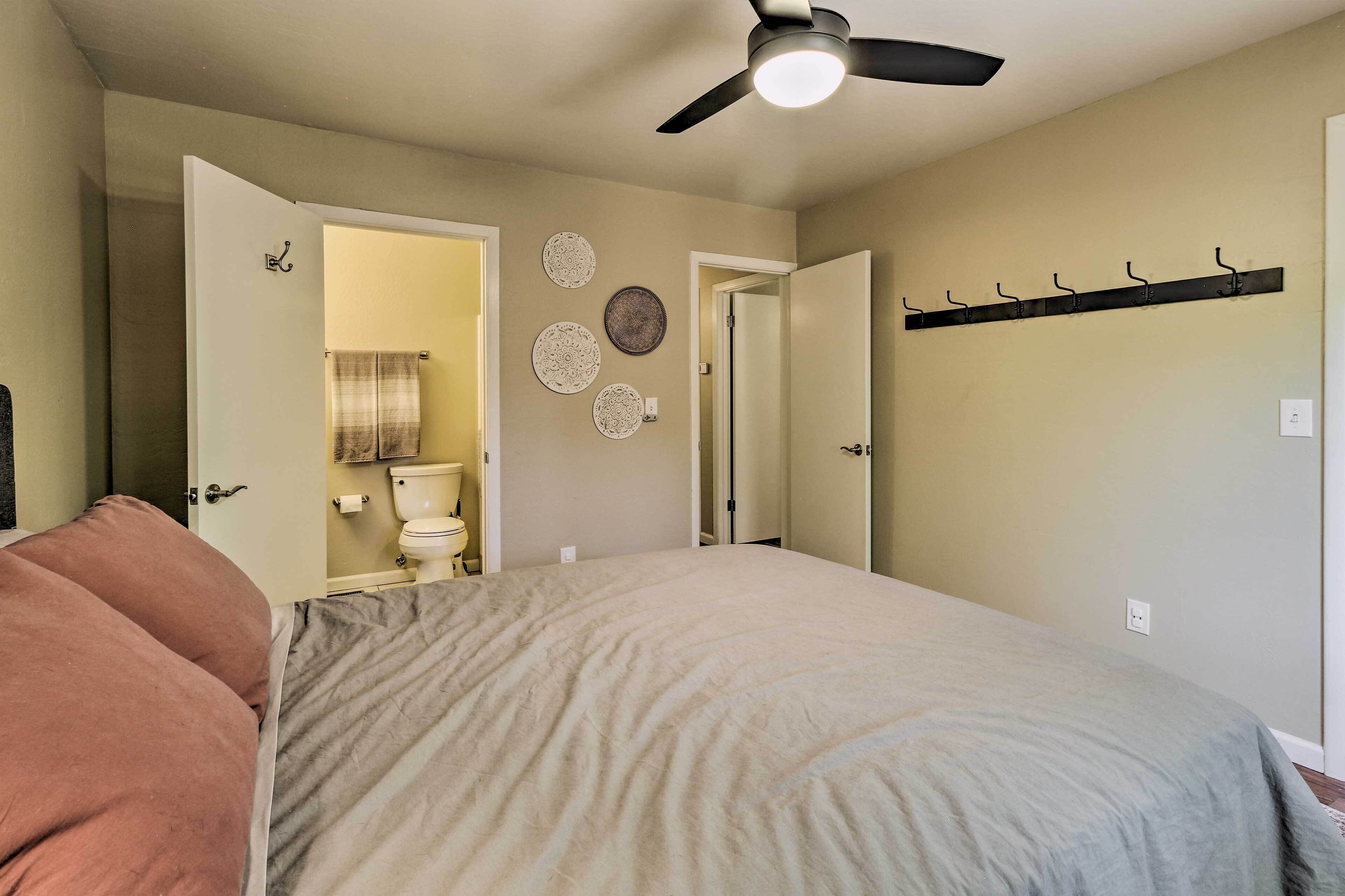 Un dormitorio con cama, ventilador de techo, perchero y un baño visible a través de una puerta abierta.