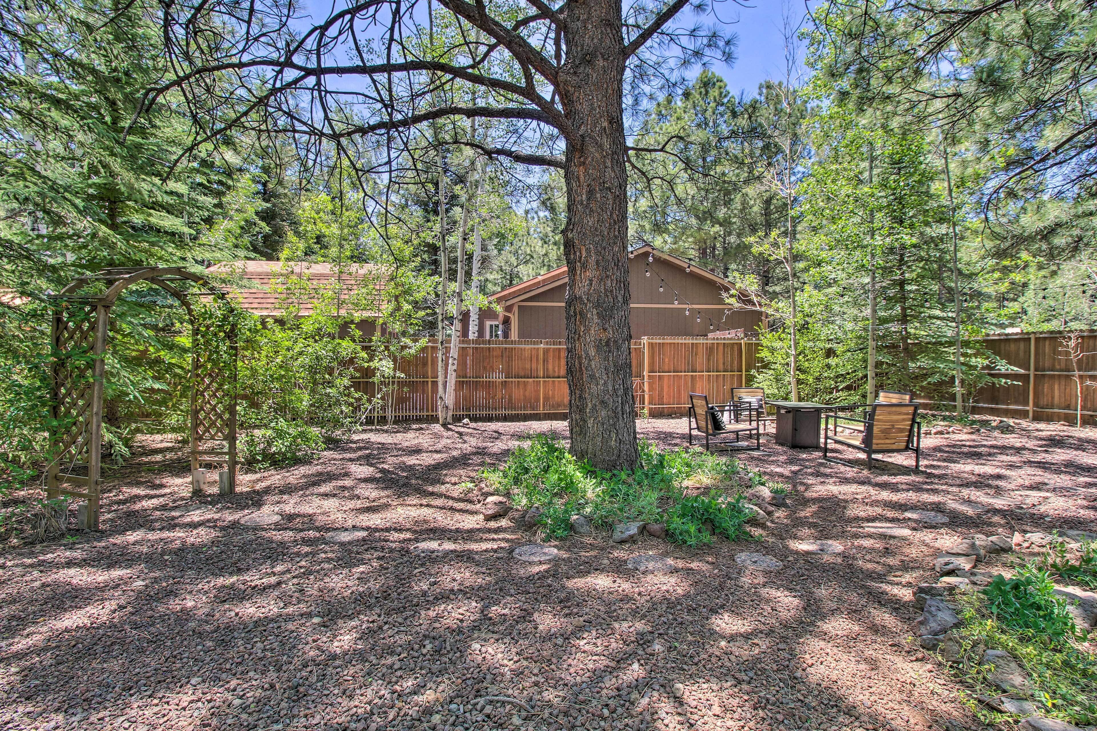 A cabin surrounded by trees with a gravel ground, a wooden deck, and a table with chairs.