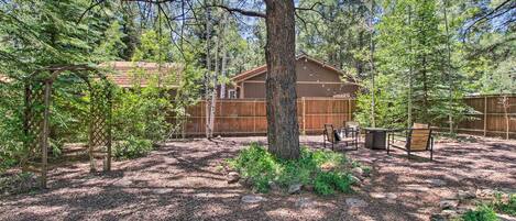 A cabin surrounded by trees with a gravel ground, a wooden deck, and a table with chairs.