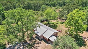 A single-story house with a metal roof, surrounded by dense forest. - Private Hot Tub & Yard: Secluded Broken Bow Home! (Broken Bow)
