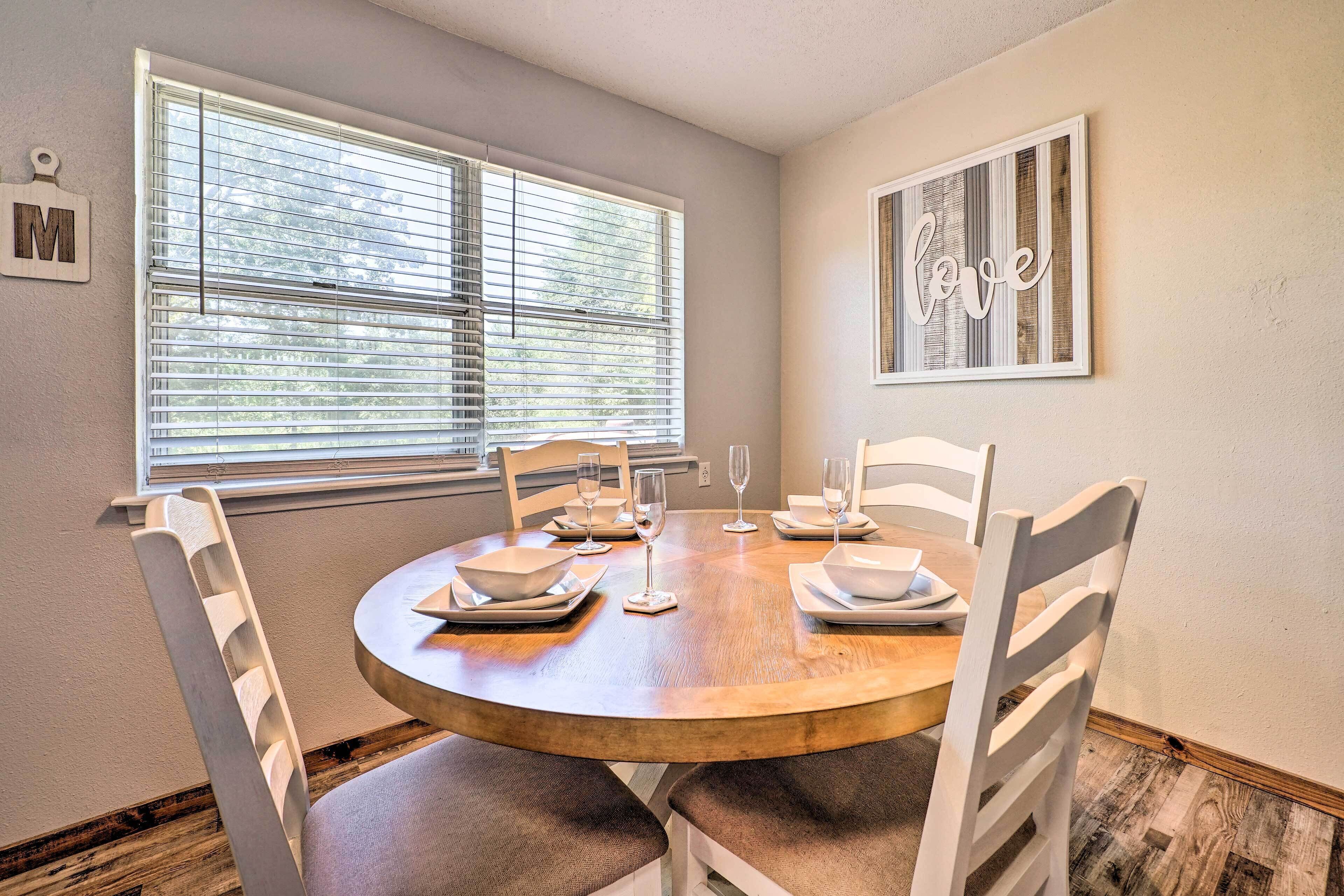 A dining area with a round wooden table, white chairs, and a window with blinds.