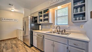 A kitchen with white cabinets, a stainless steel refrigerator, a dishwasher, and a window with blinds. - Private Hot Tub & Yard: Secluded Broken Bow Home! (Broken Bow)