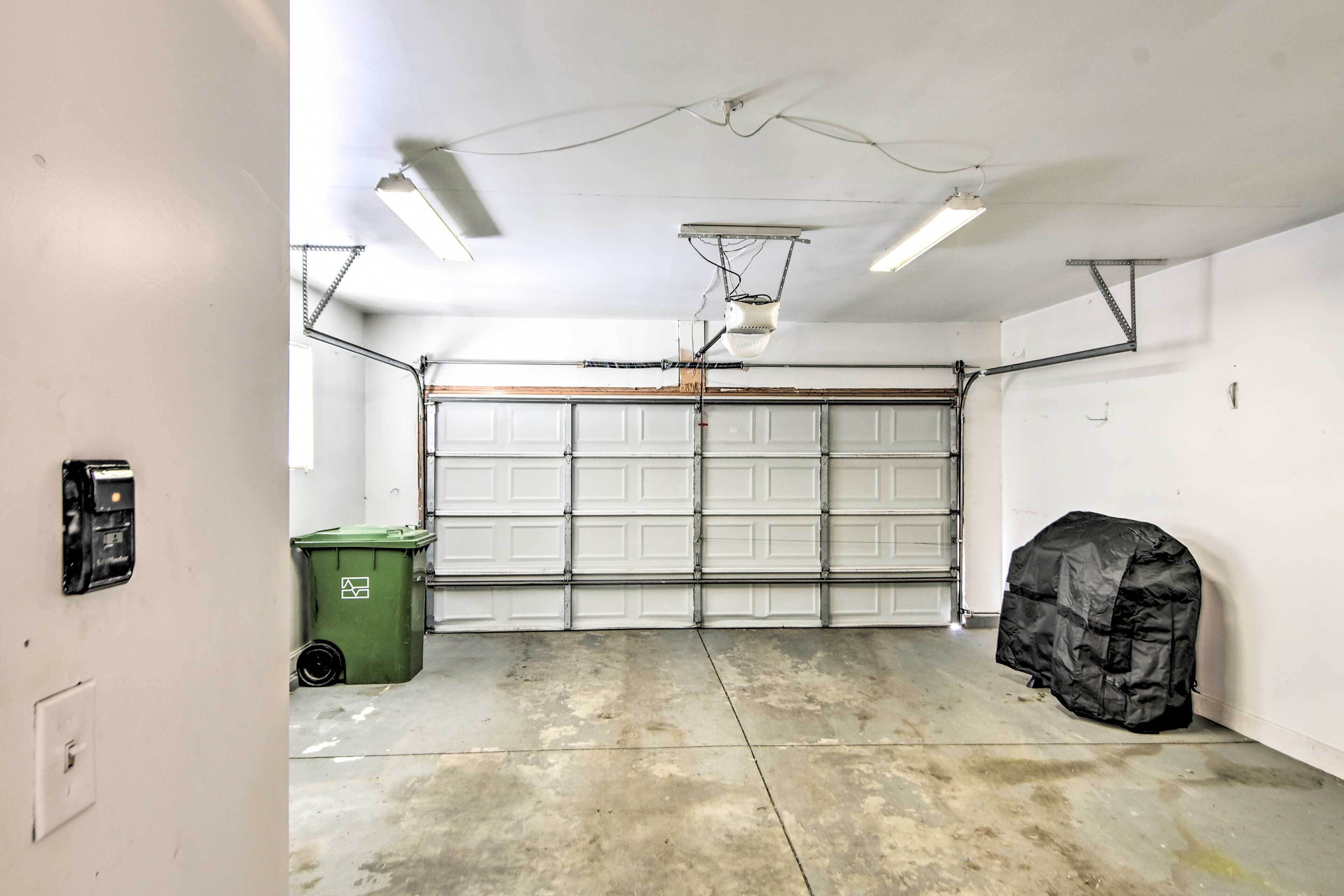 Un garage avec une porte de garage blanche, une poubelle verte et un objet noir sur le sol.