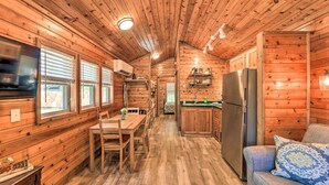 Interior de una cabaña de madera con comedor, cocina y sofá.