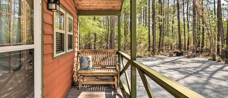 A wooden porch with a bench and a table, overlooking a forested area.