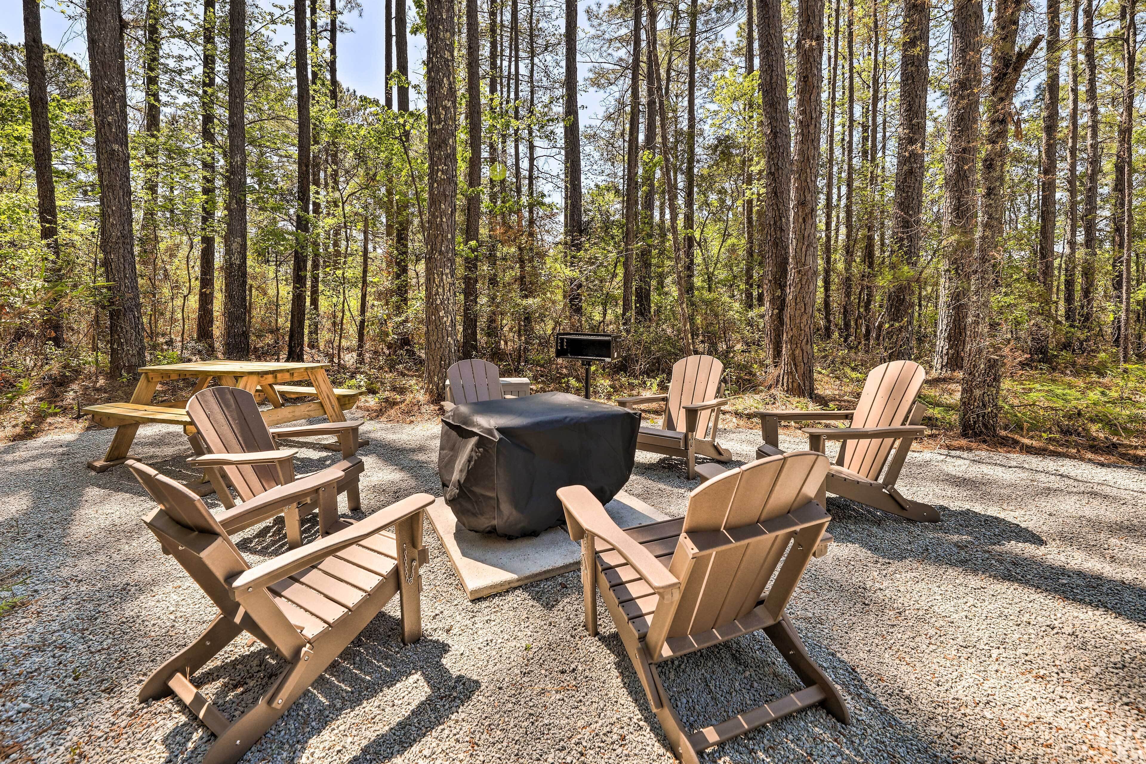A forest setting with a seating area featuring Adirondack chairs and a covered fire pit.