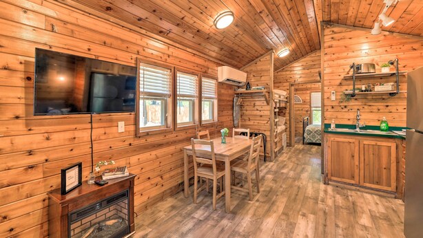 Interior de una cabaña de madera con comedor, cocina y chimenea.