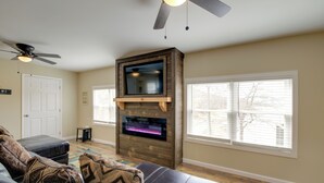 Un salon avec une cheminée, un ventilateur de plafond, une grande fenêtre et une porte.