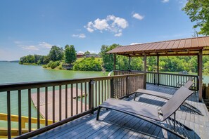 Terraza de madera con dos sillones de descanso y una pérgola con vistas a un lago.