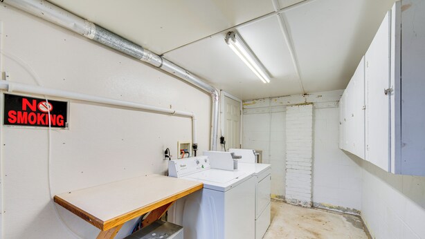 A laundry room with a no smoking sign, a washing machine, a dryer, and a wooden table. - 'schoolhouse Haven' in Gap: Communal Grill & Patio (Gap)