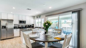 A modern kitchen with white cabinets, stainless steel appliances, and a dining area with a wooden table and chairs. - Pool & Putting Green: Scottsdale Family Escape (Scottsdale)