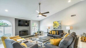 A modern living room with a fireplace, grey sofas, yellow cushions, and a large window. - Pool & Putting Green: Scottsdale Family Escape (Scottsdale)