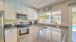 A modern kitchen with white cabinets, a granite countertop, stainless steel appliances, and a large window offering a view of the outdoors. - Pool & Putting Green: Scottsdale Family Escape (Scottsdale)