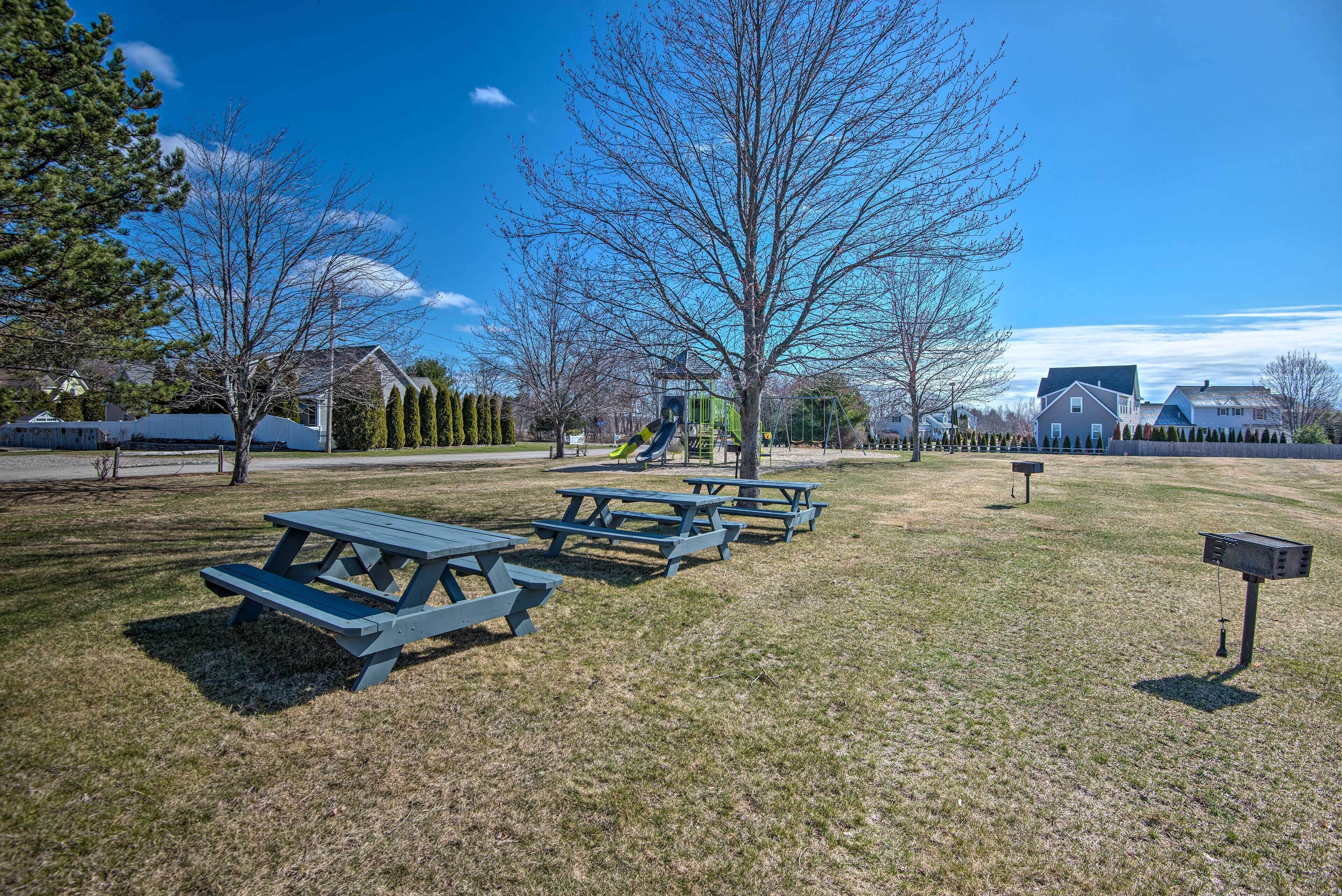 A park with picnic tables, playground equipment, and a clear blue sky.