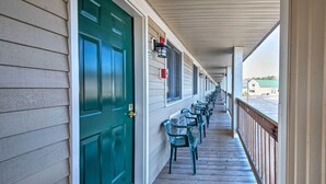 A covered porch with a green door, rows of chairs, and a view of the street. - Southern Maine Retreat < 2 Mi to Wells Beach! (Wells)