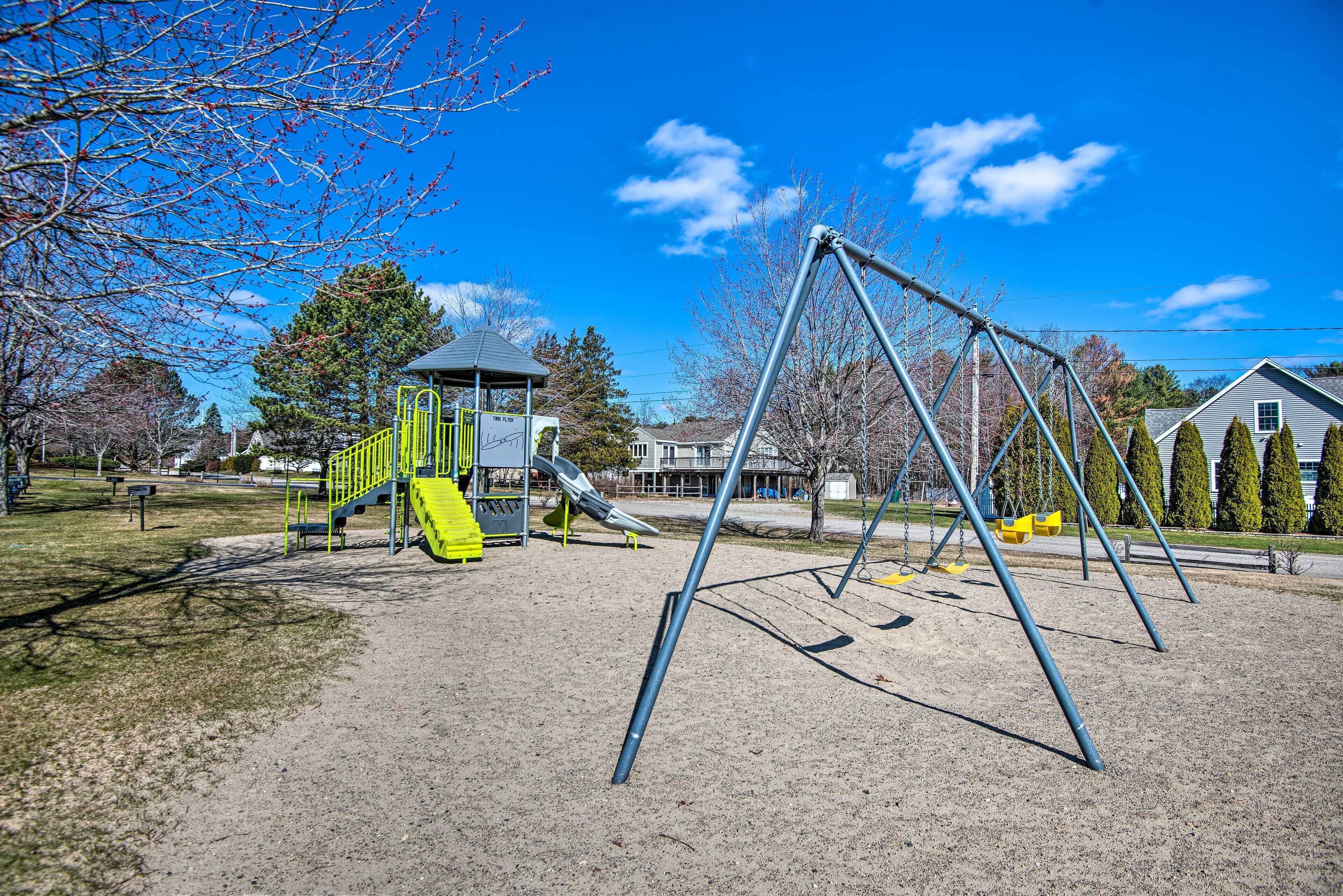 A playground with swings and a slide, surrounded by trees and houses.