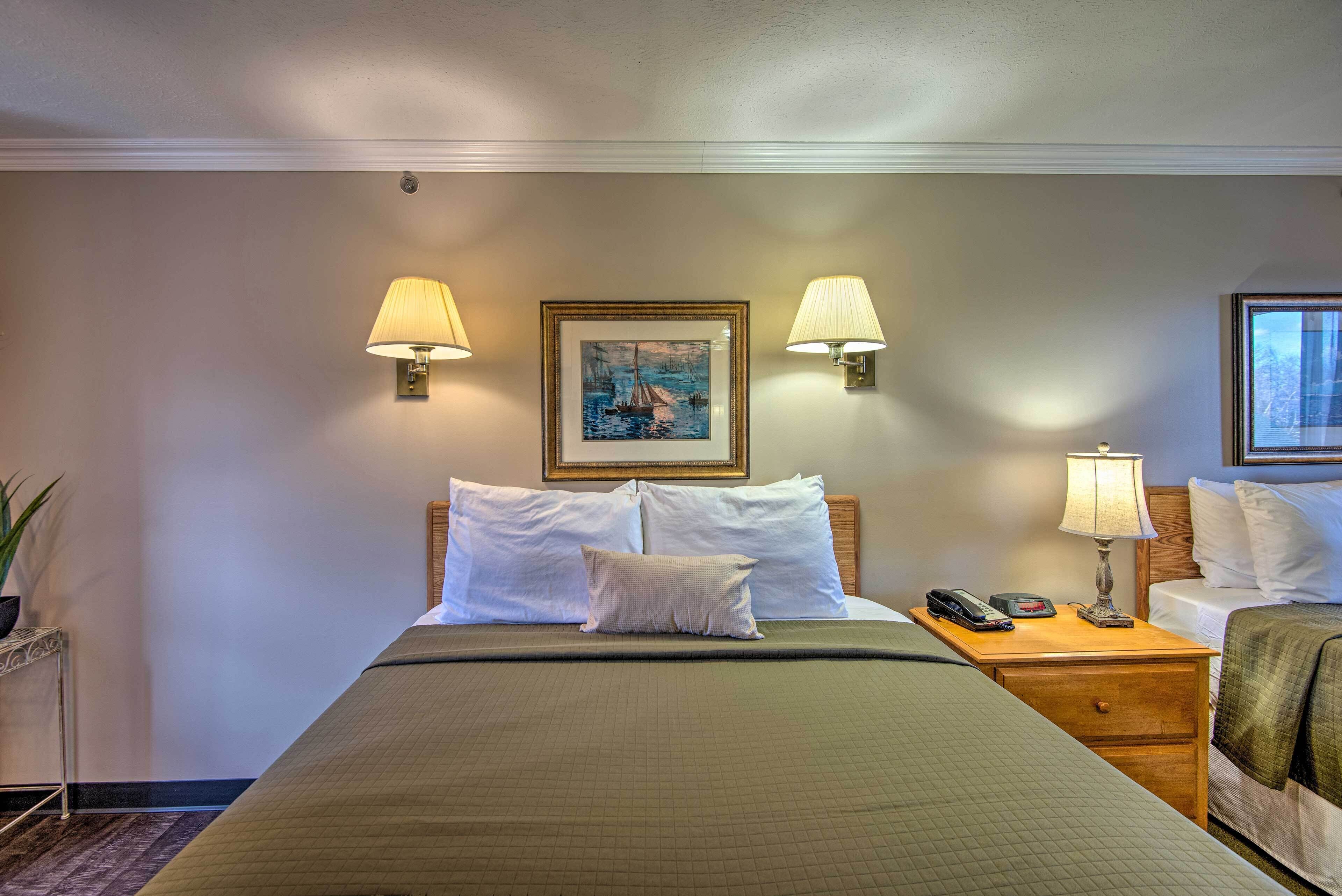 A hotel room with a large bed, two bedside lamps, a painting on the wall, and a nightstand with a phone and lamp.