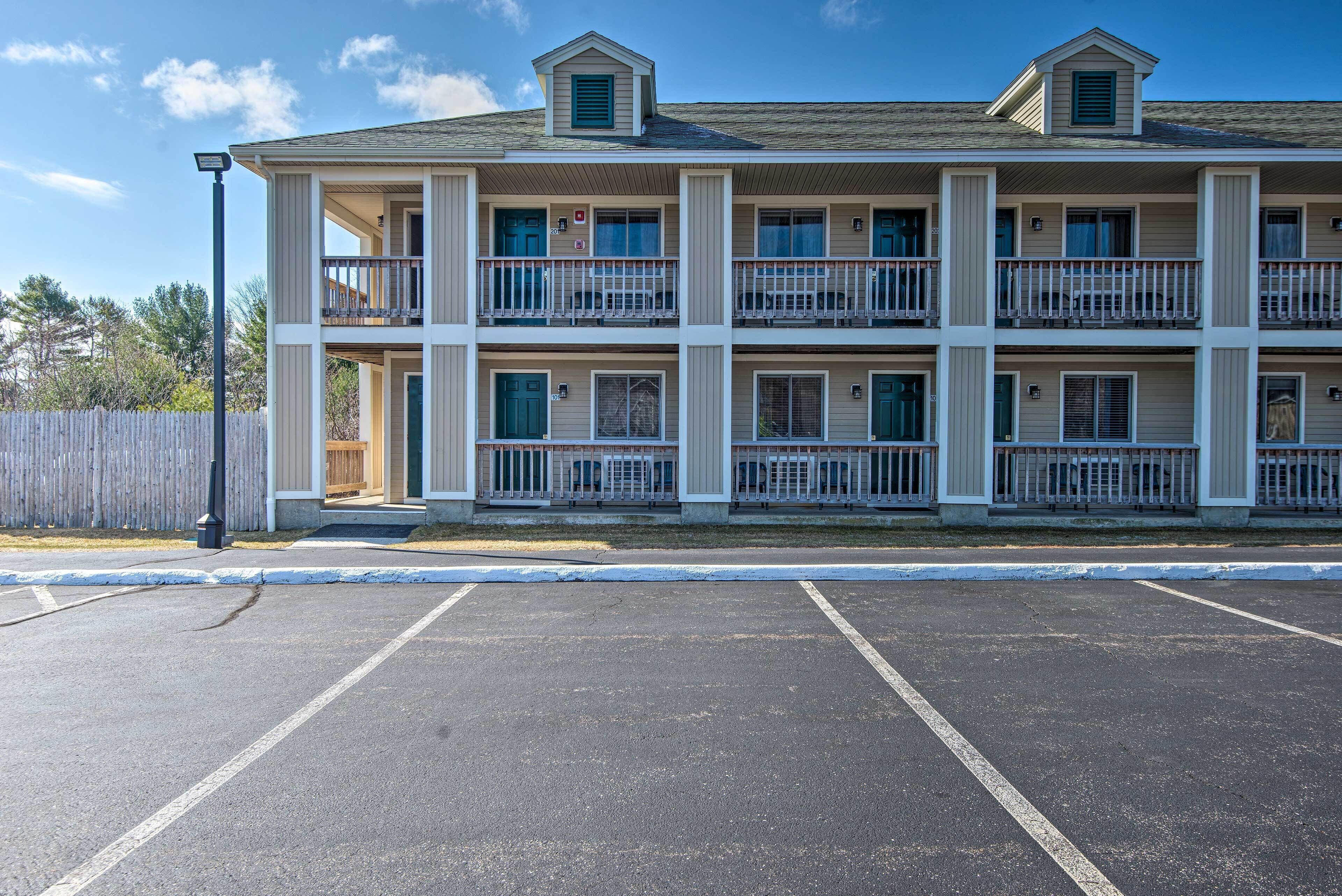 A multi-story motel with balconies, a parking lot, and a wooden fence in the background.