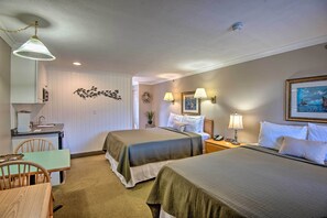 Een hotelkamer met twee bedden, een bureau en een stoel. Er is een kleine kitchenette met een spoelbak en een kookplaat.
