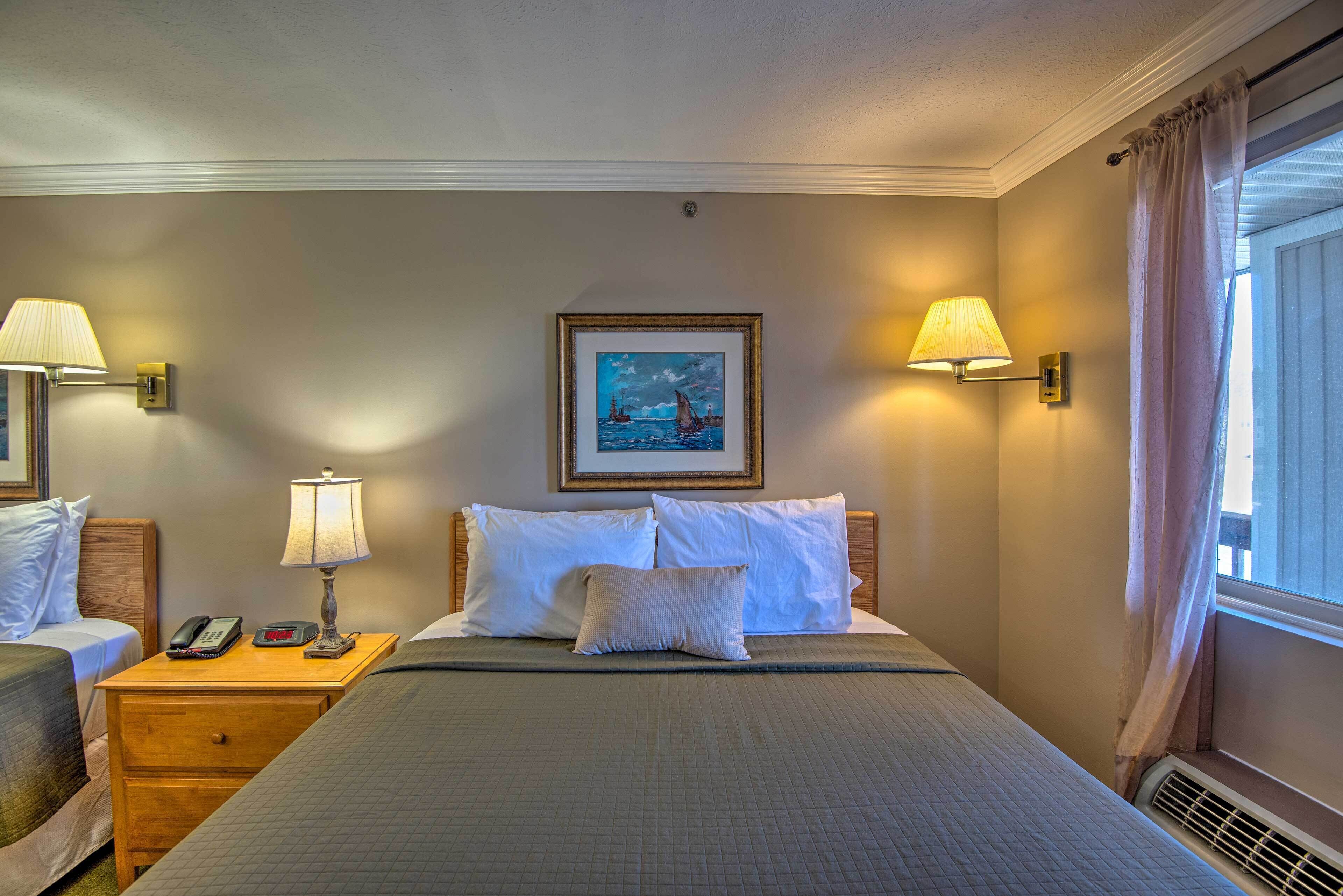 Una habitación de hotel con una cama grande, dos mesitas de noche con lámparas, un cuadro en la pared y una ventana con cortinas.