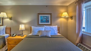 Una habitació d'hotel amb un llit gran, dues taules de nit amb làmpades, un quadre a la paret i una finestra amb cortines.