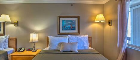 A hotel room with a large bed, two bedside tables with lamps, a painting on the wall, and a window with curtains.